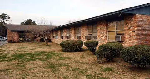 Brick, single-story facility exterior with windows, a covered entry, and trimmed shrubs.