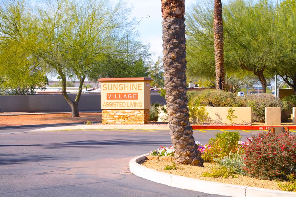 Entrance sign reading 'Sunshine Village Assisted Living' beside palm trees and a landscaped roundabout.