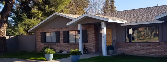 Single-story brick house front with a covered porch, potted plants, and the address number 707.