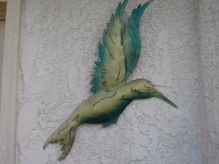 Colorful hummingbird wall sculpture mounted on a textured exterior wall.
