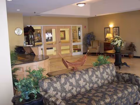 Warm lobby area with patterned sofa, plants, a reception desk, and double doors.