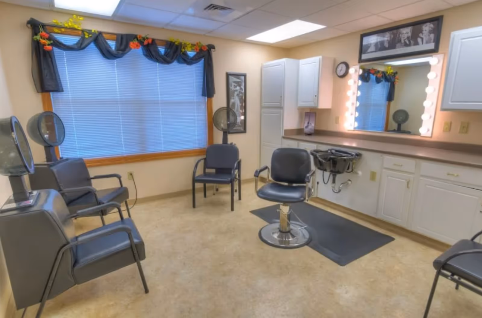 Interior salon room with styling chairs, a shampoo sink, an illuminated mirror, and seating by a large window.