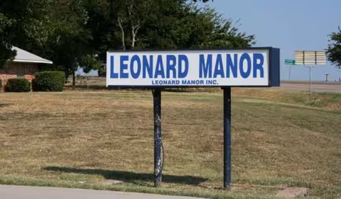 A Leonard Manor sign on a grassy lot beside a road