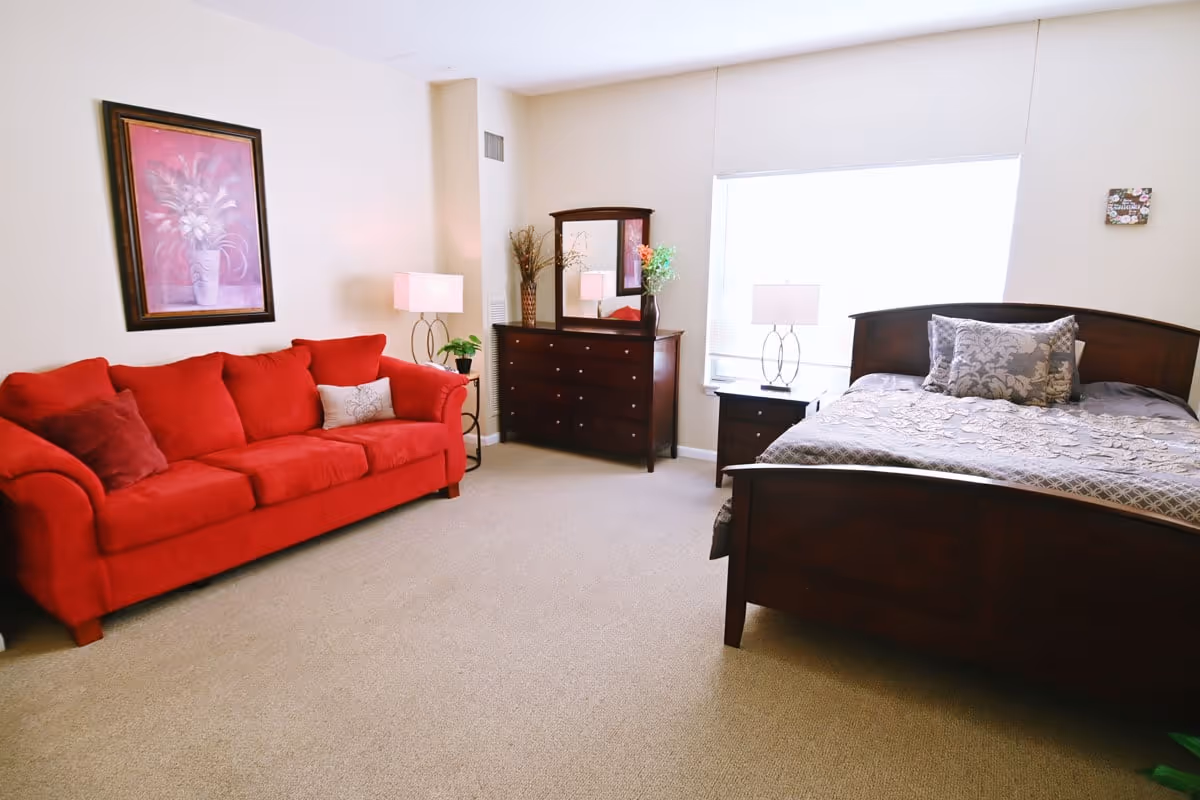 Well-lit furnished bedroom with a red sofa, wooden bed and dresser, and bedside lamps.