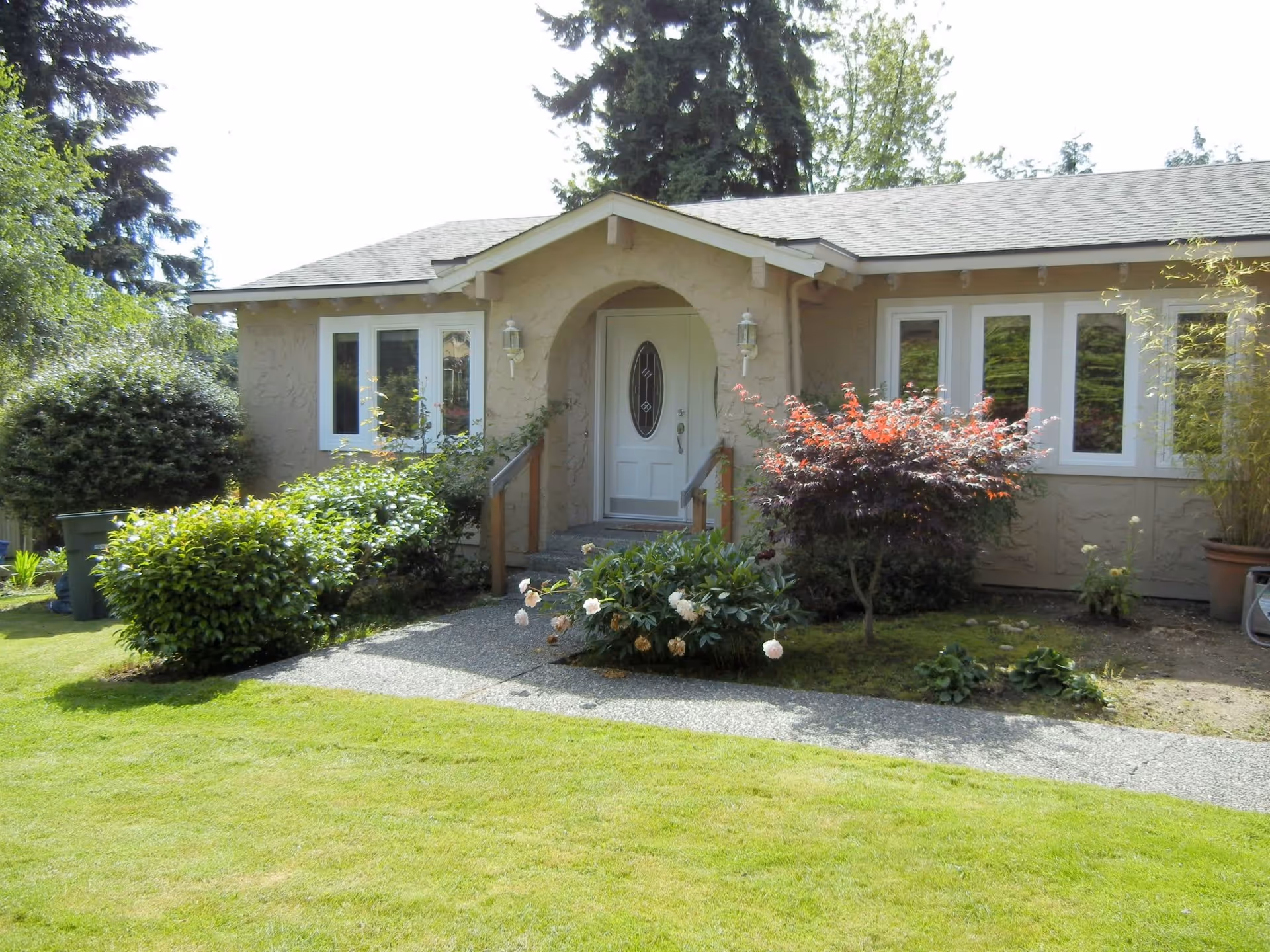 Front exterior of a single-story house with a lawn, shrubs, and a centered front door with a small porch.