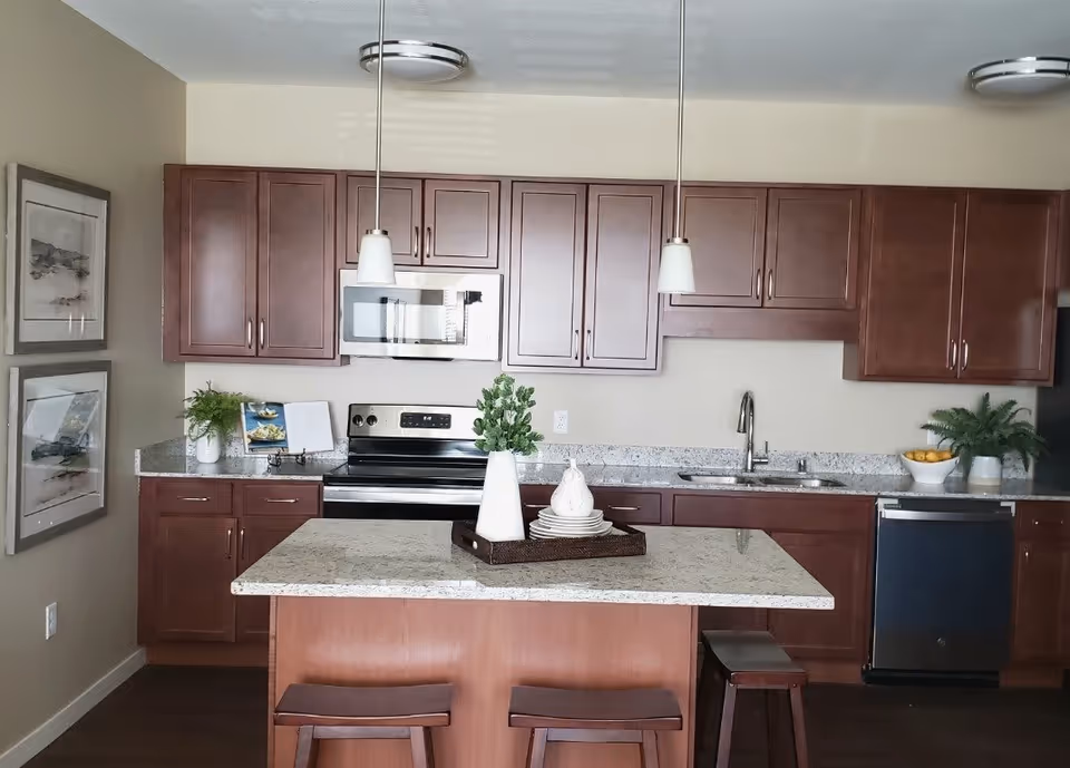 Modern kitchen with a granite island, pendant lights, stainless steel appliances, and wooden cabinets.