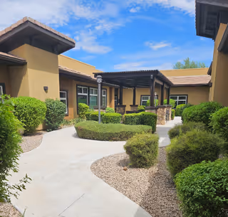 Exterior view of Mosaic Gardens Memory Care at Chandler with walkway and manicured shrubs.