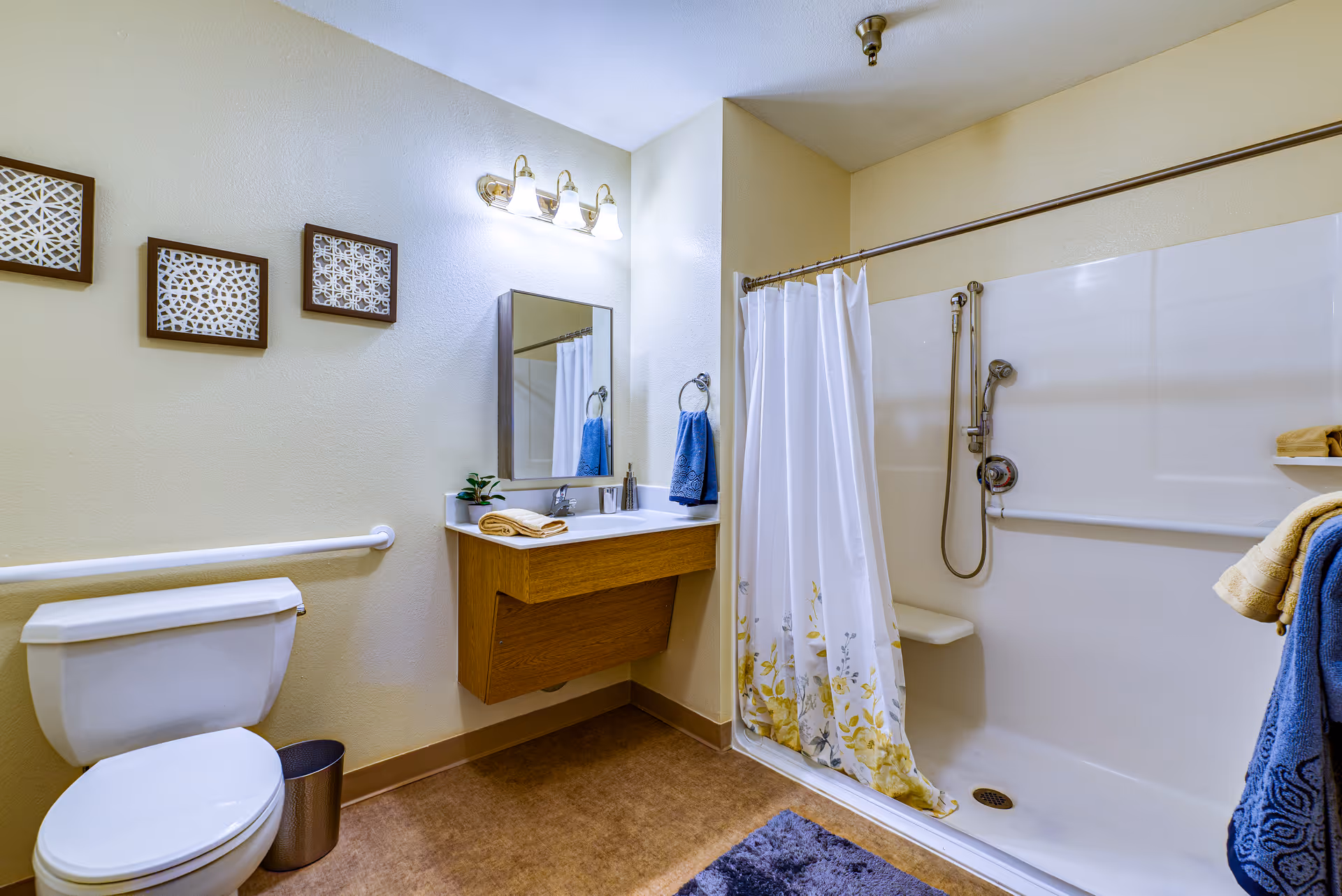 Accessible bathroom with a toilet, wall-mounted sink and mirror, and a bathtub/shower with a curtain and grab bars.