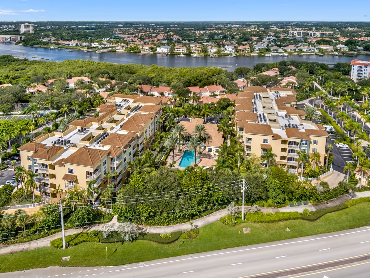 Aerial view of Riverwalk Pointe complex showing multiple residential buildings around a central pool, lush landscaping, and a river in the background.