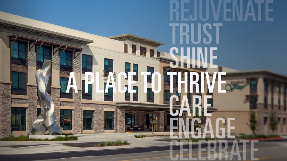 Exterior view of Belmont Village Senior Living Albany building with a modern design featuring stone and beige walls, large windows, and a metal sculpture in front. Text overlay reads 'A PLACE TO THRIVE' along with words like REJUVENATE, TRUST, SHINE, CARE, ENGAGE, and CELEBRATE.