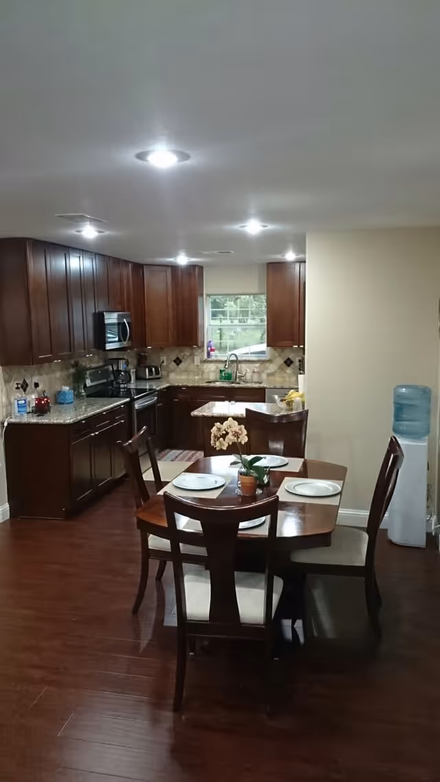 Open kitchen with dark wood cabinets, a small island, and a dining table set for four in the foreground.