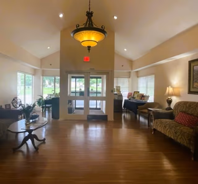 Spacious furnished lobby with hardwood floors, seating, and double glass entrance doors under a hanging chandelier.