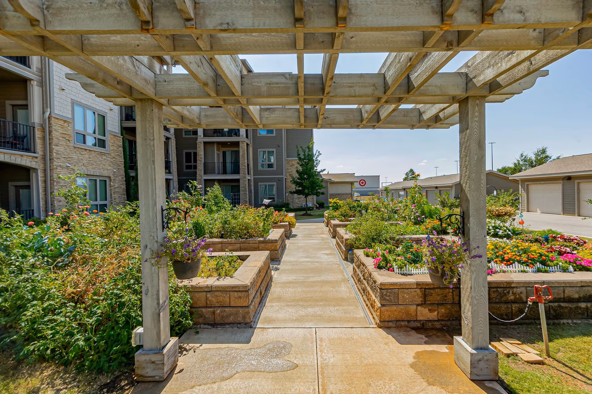 Wooden pergola over a paved walkway flanked by raised flower beds and gardens between apartment buildings.