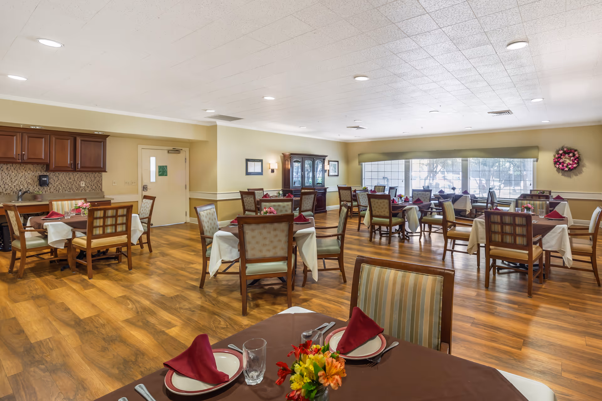 Well-lit dining room with multiple set tables and wooden chairs, buffet cabinets, and large windows.