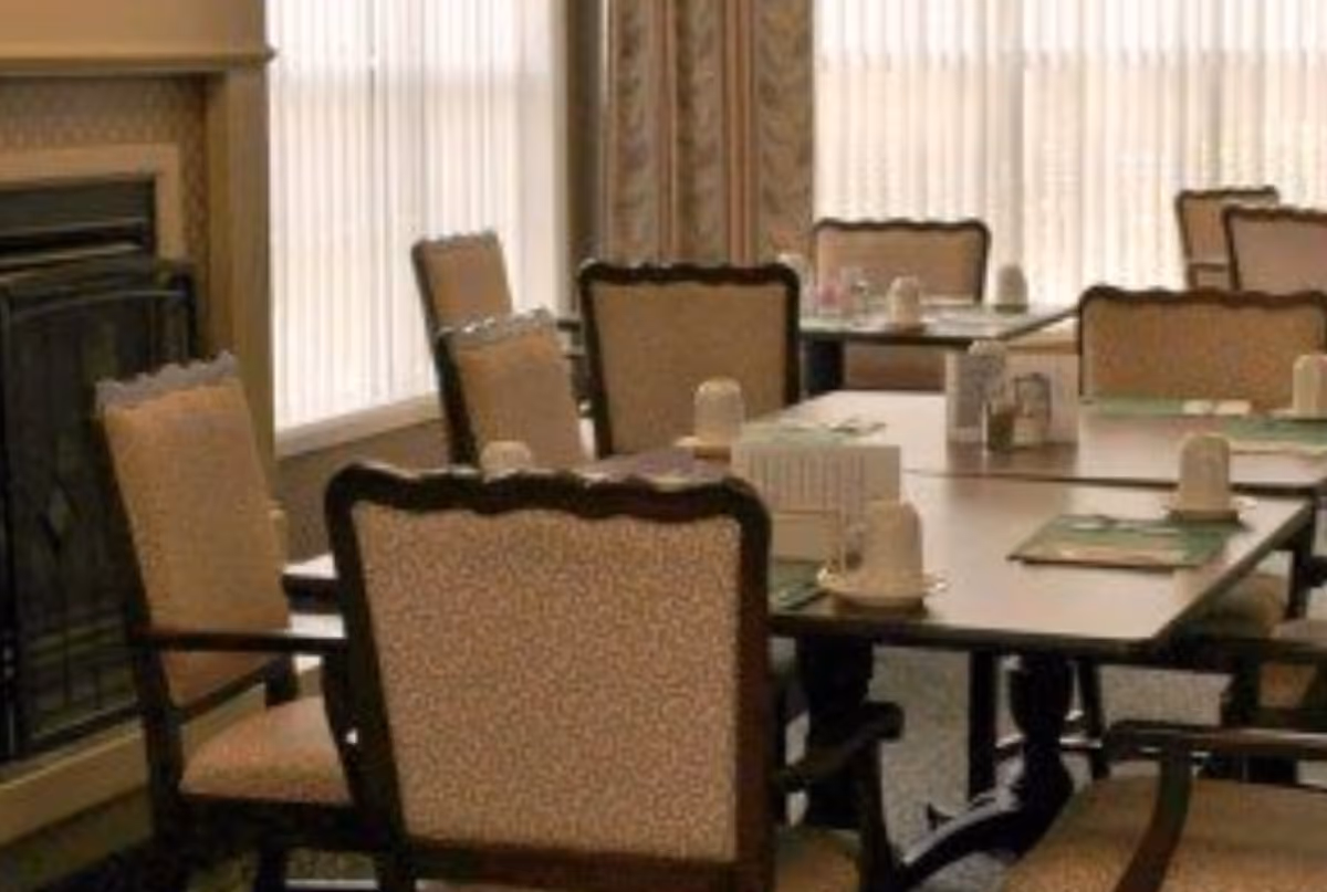 A dining room with multiple tables set with cups and place mats surrounded by upholstered chairs.
