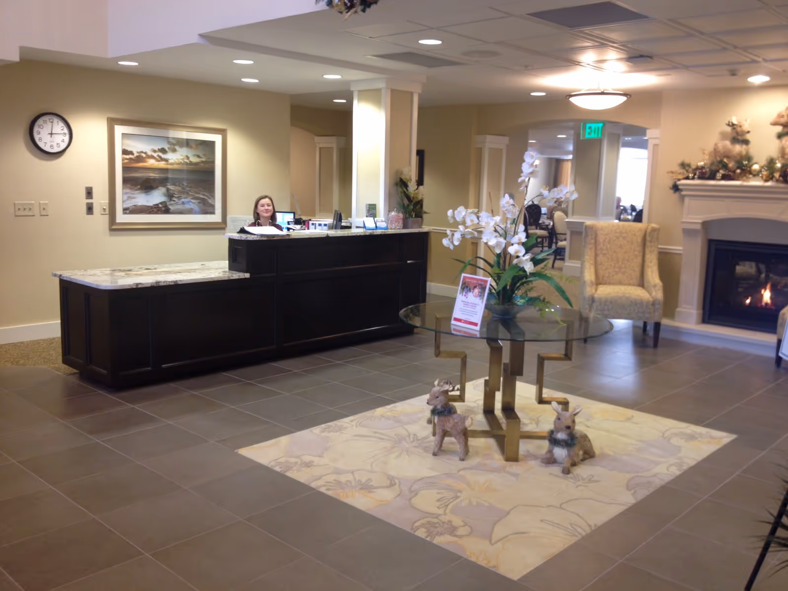 Reception lobby with a front desk, glass table with flowers, seating area and a fireplace.