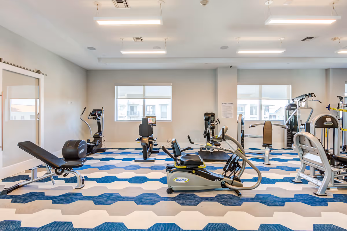 Bright fitness room with exercise machines and benches on a blue-and-white patterned floor.