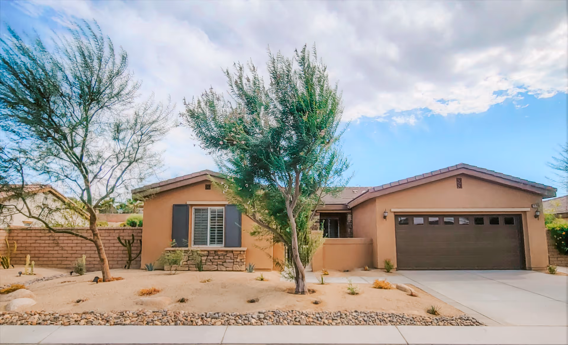 Front exterior of a single-story stucco house with a two-car garage, driveway, and desert landscaping.