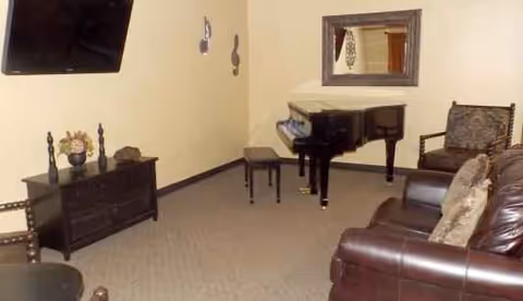 Cozy living room in a senior facility with a piano, leather seating, and a wall mirror.