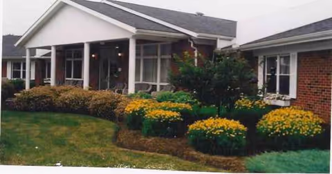 Front exterior of Logan Elm Health Care Center with yellow flowering shrubs and a walkway.