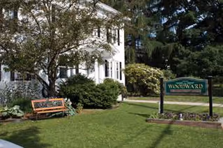 White two-story facility with a manicured lawn, trees, and a wooden bench outdoors.