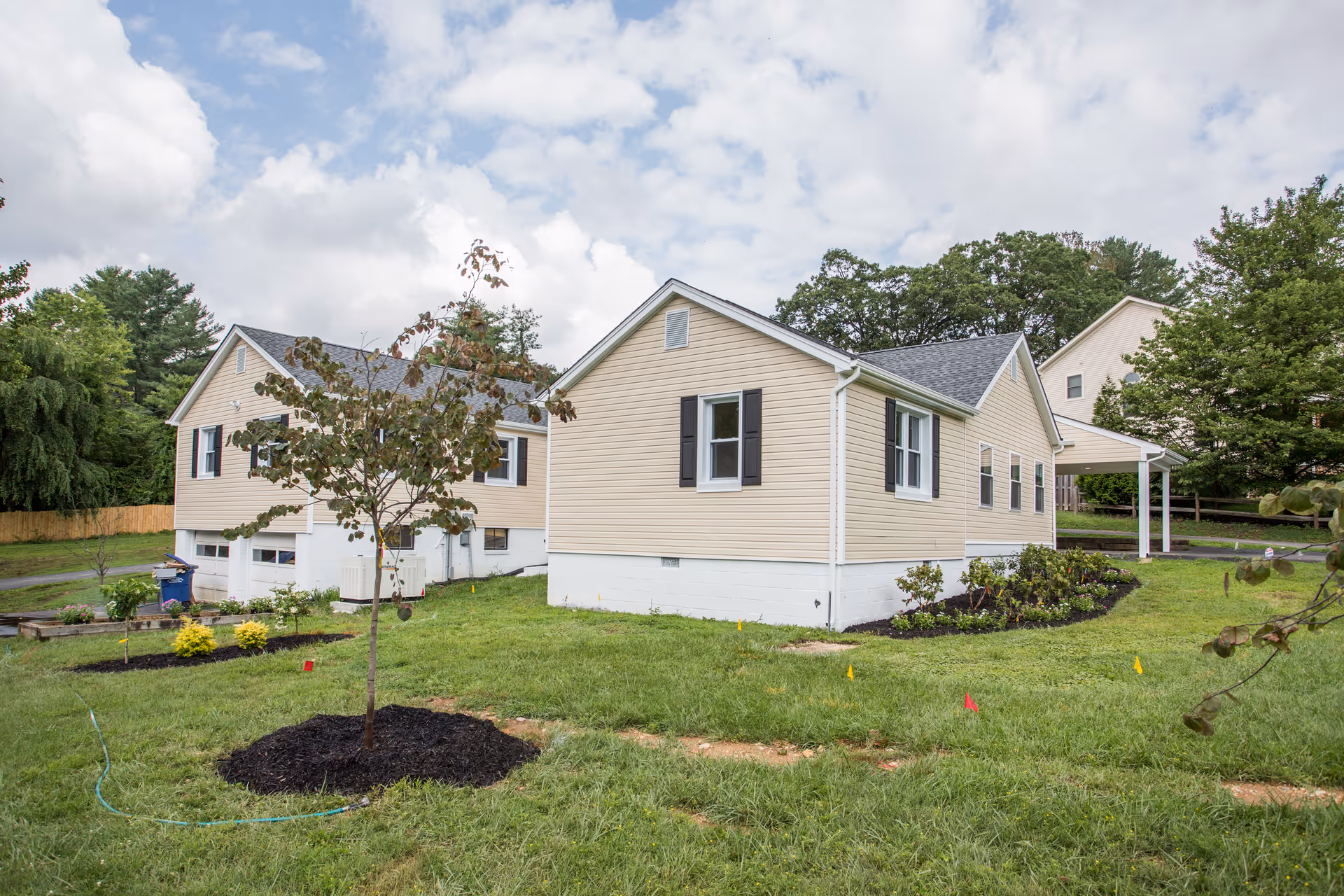 Beige single-story assisted living building with a lawn, young trees, and landscaped beds under a cloudy sky.