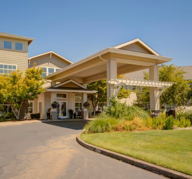 Front entrance of a senior living building with a covered porte-cochere, driveway, and landscaped lawn.