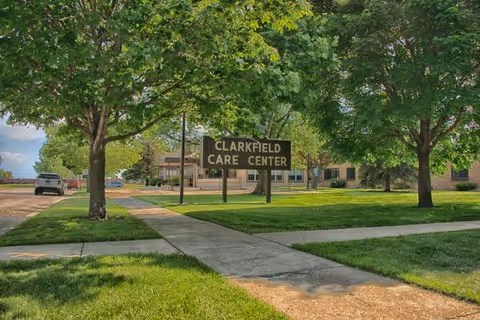 Front view of the Clarkfield Care Center entrance sign surrounded by trees.