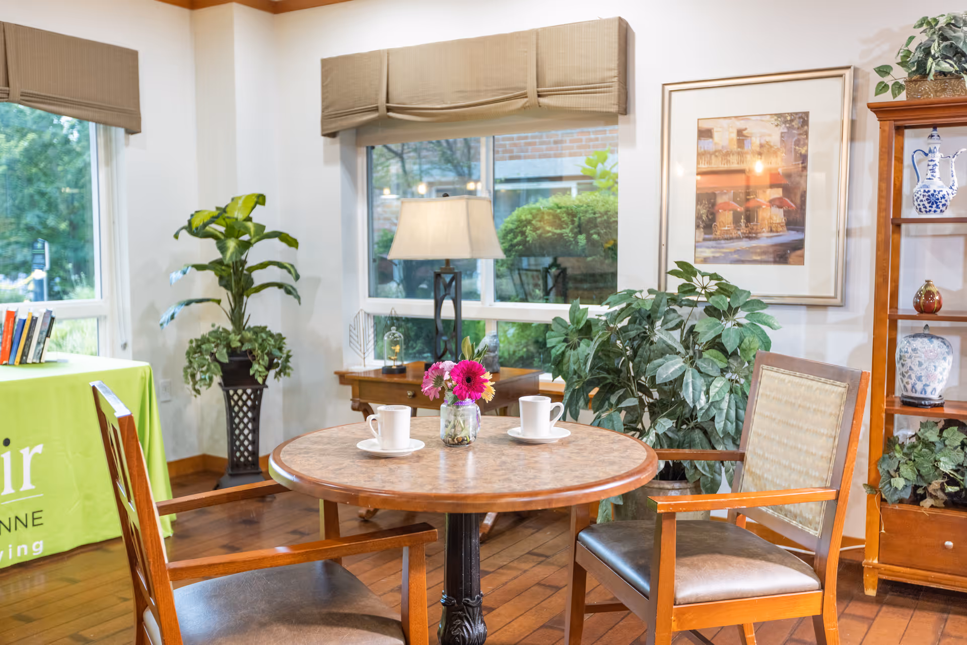 A cozy seating area with a table, two chairs, a lamp, plants, and a decorative shelf.