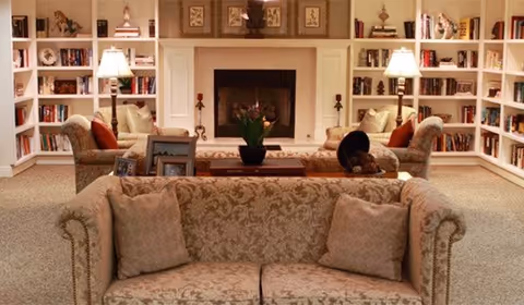 Cozy living room with patterned sofas facing a central fireplace, flanked by built-in bookshelves and table lamps.