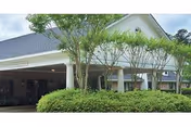 Covered entrance of a light-colored nursing and rehabilitation building with columns, trees, and shrubs.