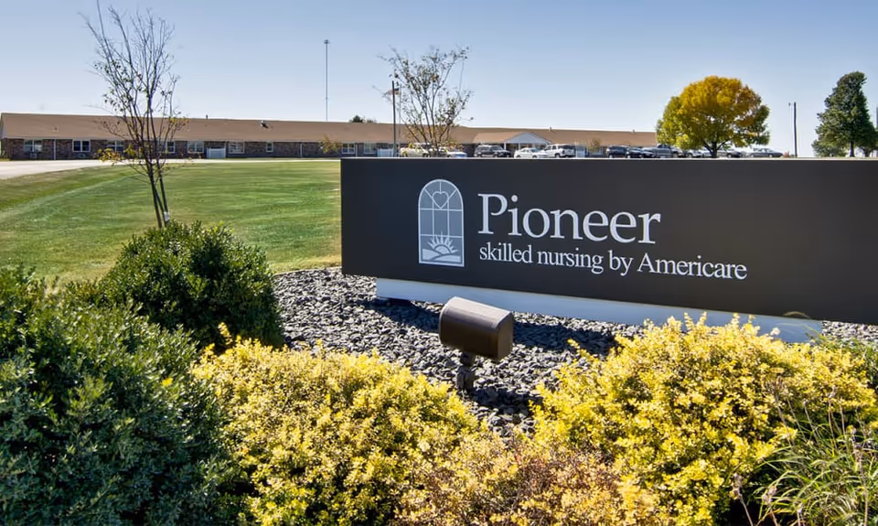 Exterior view of a 'Pioneer skilled nursing by Americare' sign on a landscaped lawn with the facility building in the background.