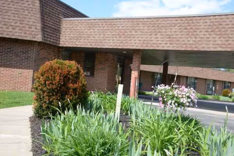 Brick senior living facility exterior with landscaped shrubs and flowering plants near the entrance.