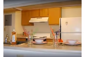 Interior view of a senior apartment kitchen with wooden cabinets, a white refrigerator, a stove with a range hood, and a countertop set with two place settings including bowls and glasses with flowers.
