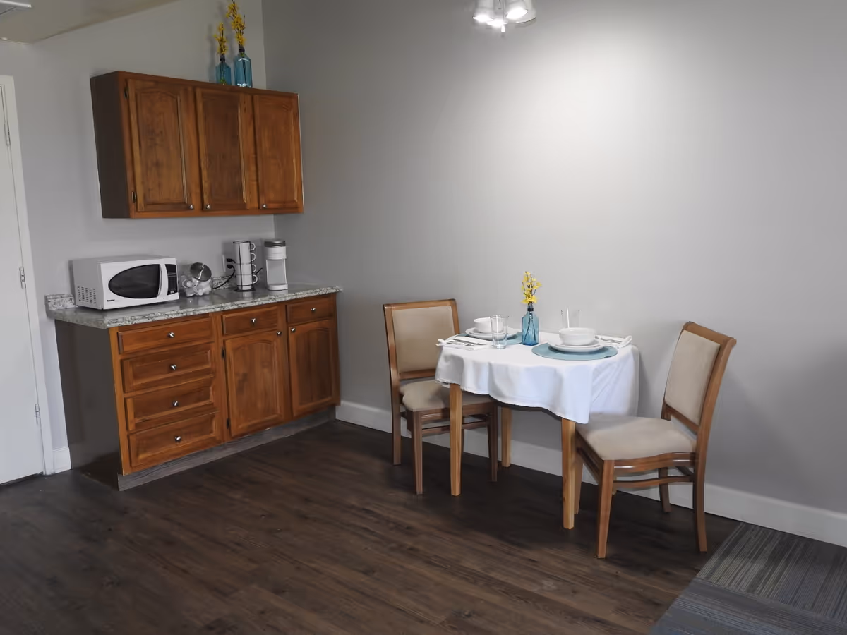 Small dining nook with a round table set for two beside wooden cabinets and a microwave.