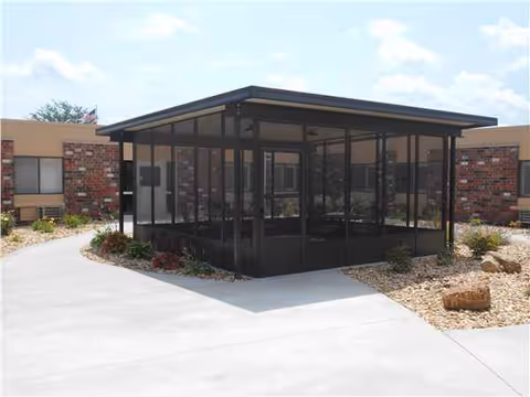 Glass-walled pavilion in a courtyard outside Warrenton Manor, with brick buildings and gravel landscaping.