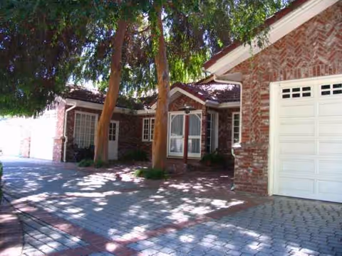 Brick senior living facility exterior with driveway, trees, and a white garage door.