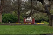 A landscaped outdoor area with green grass, trees, and flowering plants surrounding a sign that reads 'Lima Estates'.