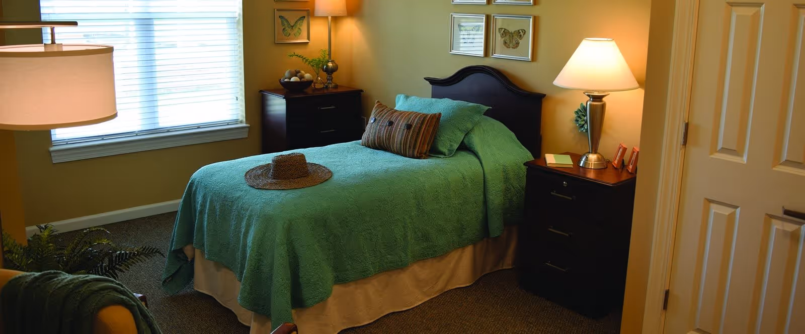Well-lit bedroom with a single bed covered in a green bedspread, two nightstands with lamps, and a window.