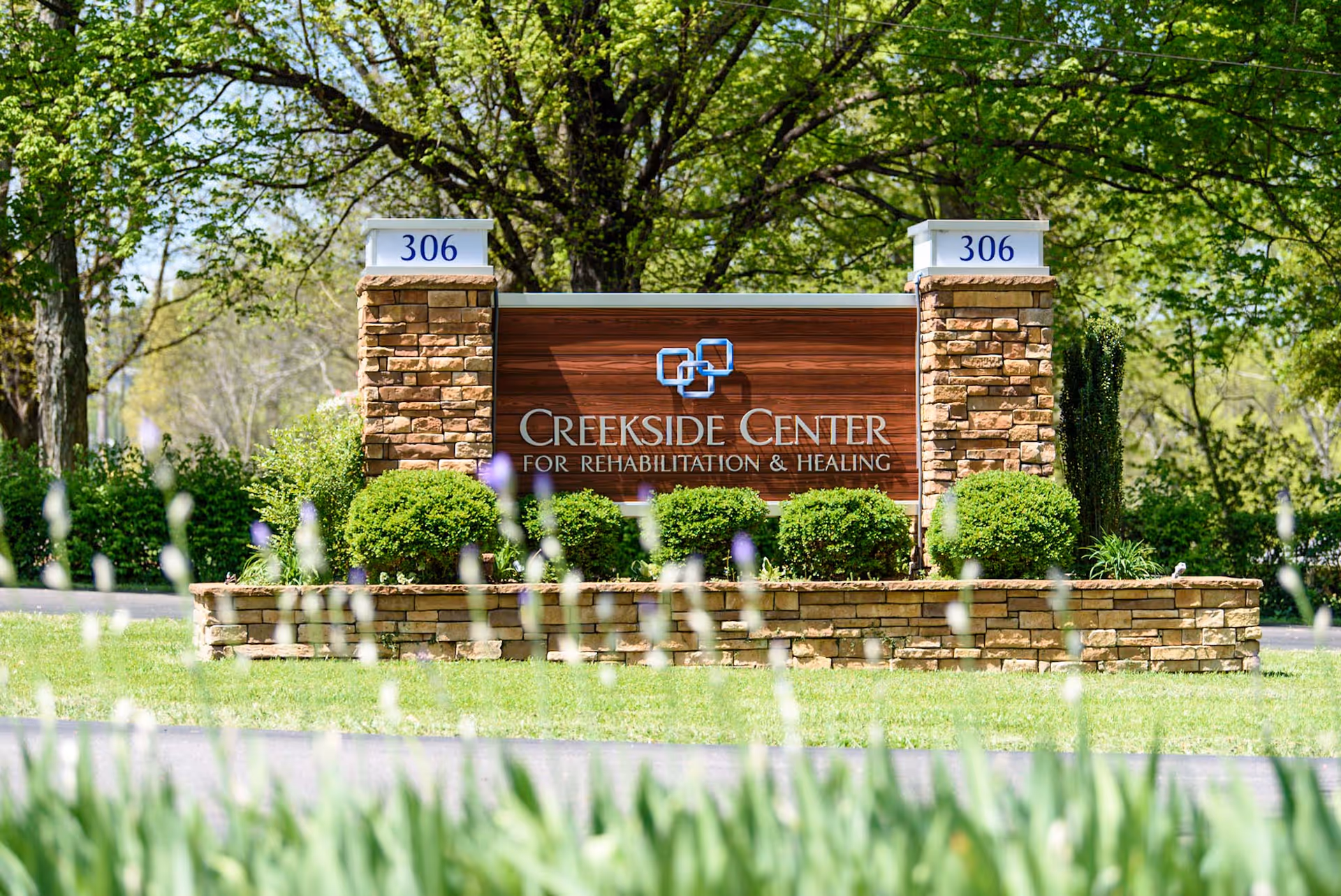 Stone and wood entrance sign reading "Creekside Center for Rehabilitation & Healing" surrounded by landscaped shrubs and trees.