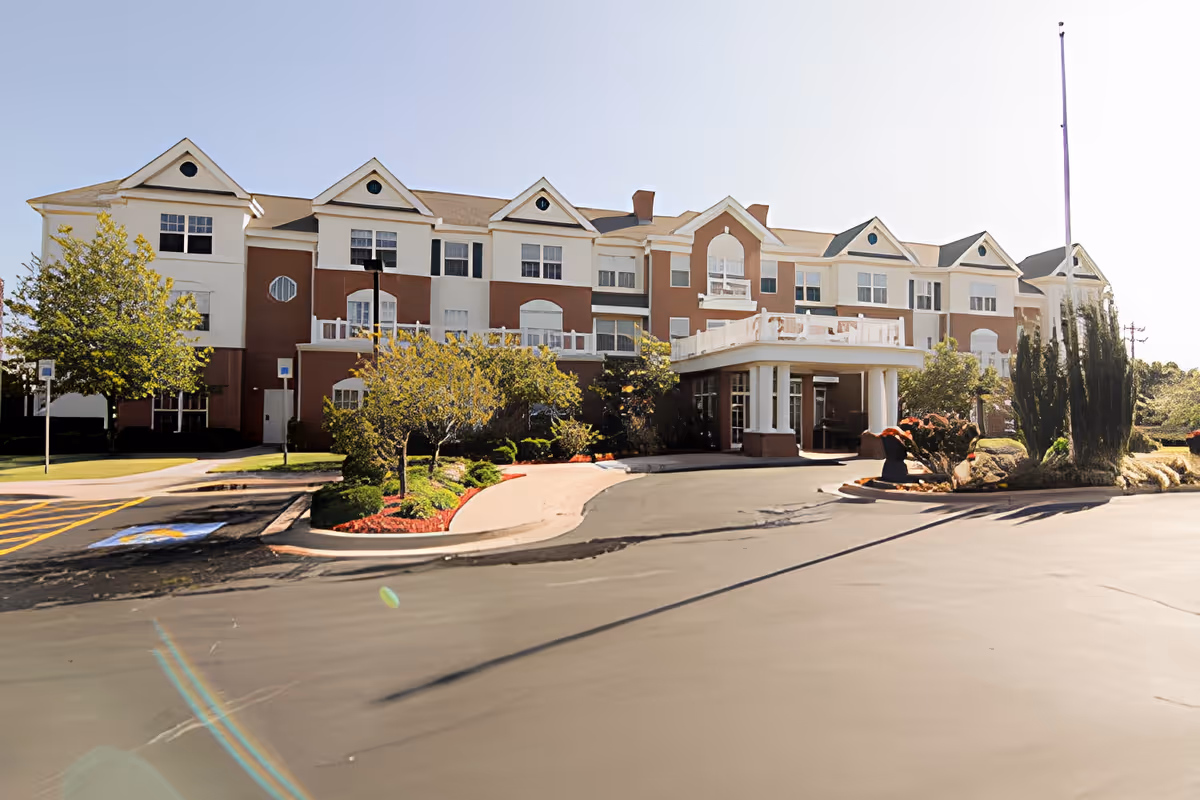 Front exterior of the Town Village senior living building with a porte-cochere entrance, landscaped driveway, and three-story façade.
