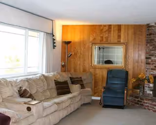 Cozy living room with beige sofa, blue recliner, brick fireplace, and wood-paneled wall.