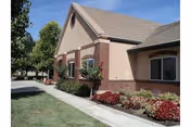 Front exterior of a single-story brick-and-stucco building with landscaped flower beds, a sidewalk, and trees under a blue sky.