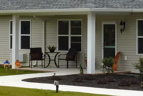 Covered front porch with two chairs, a round table, and decorative items.