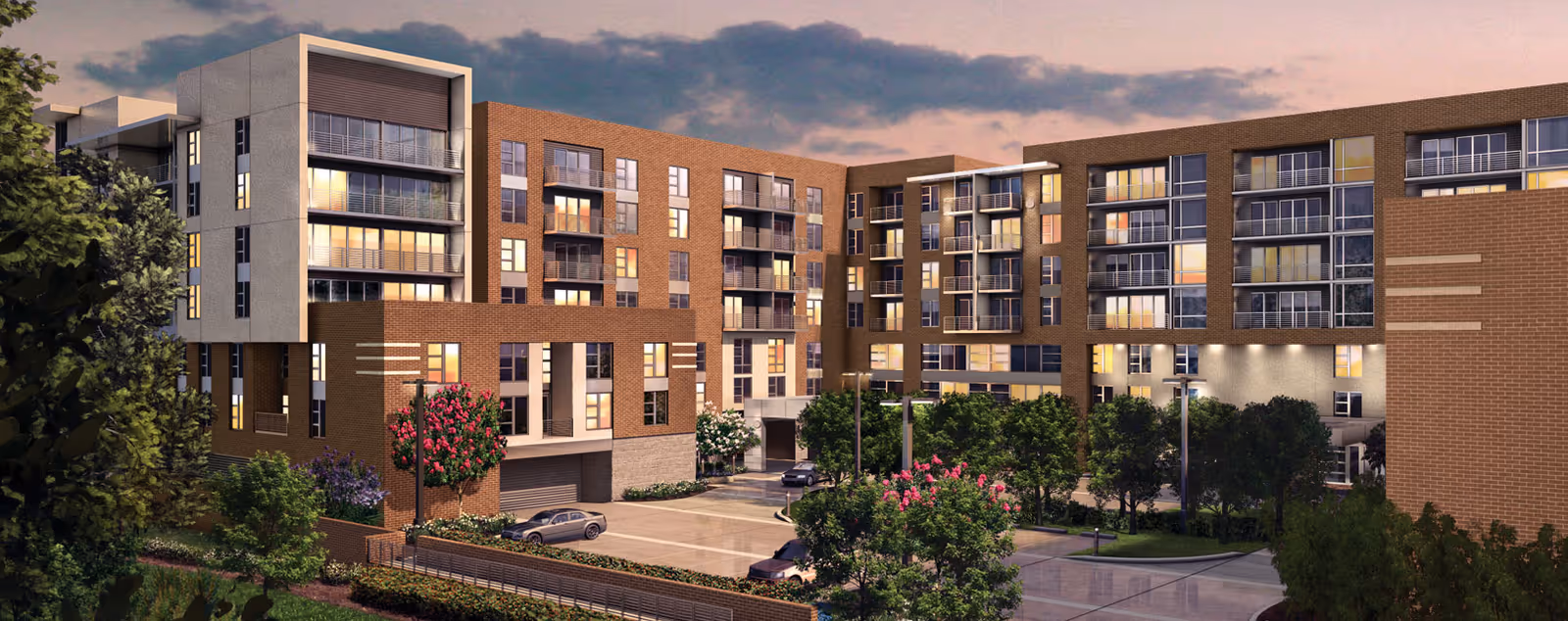 Exterior view of a modern multi-story senior living facility building at dusk with large windows, balconies, landscaped greenery, and parked cars in the driveway.