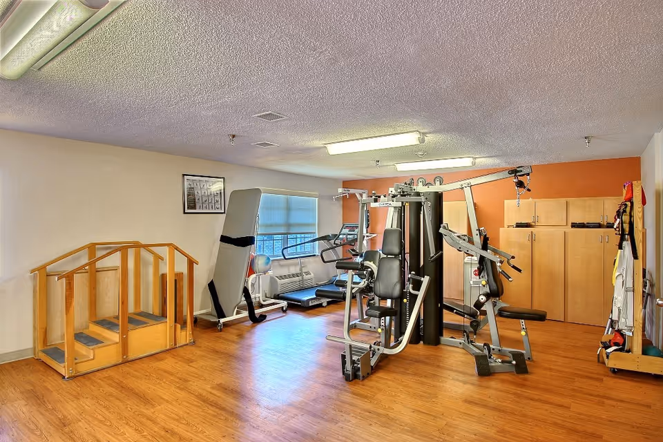 An interior exercise room with multi-station weight equipment, a treadmill, therapy stairs and storage cabinets.