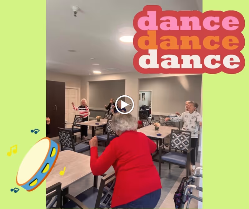 A group of elderly women dancing and exercising in a common room with tables and chairs. One woman in a red sweater is in the foreground, and others are spread around the room. The room has neutral-colored walls and ceiling lights. There are colorful graphic overlays including the words 'dance dance dance' and a tambourine with musical notes.