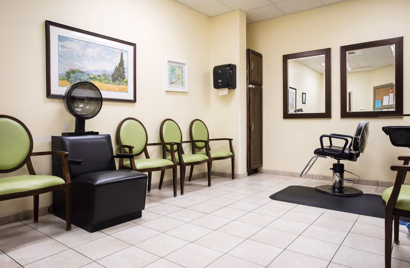 Interior salon and waiting area with green-upholstered chairs, a hair dryer station, and a styling chair in front of mirrors.