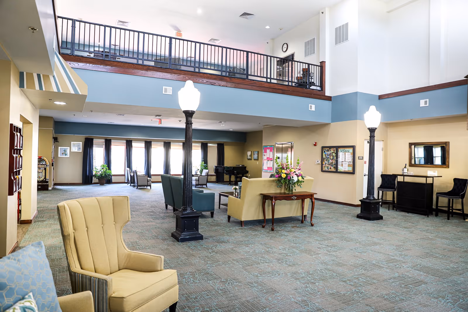 Spacious two-story senior living lobby with seating areas, decorative lampposts, and a balcony overlooking the common area.