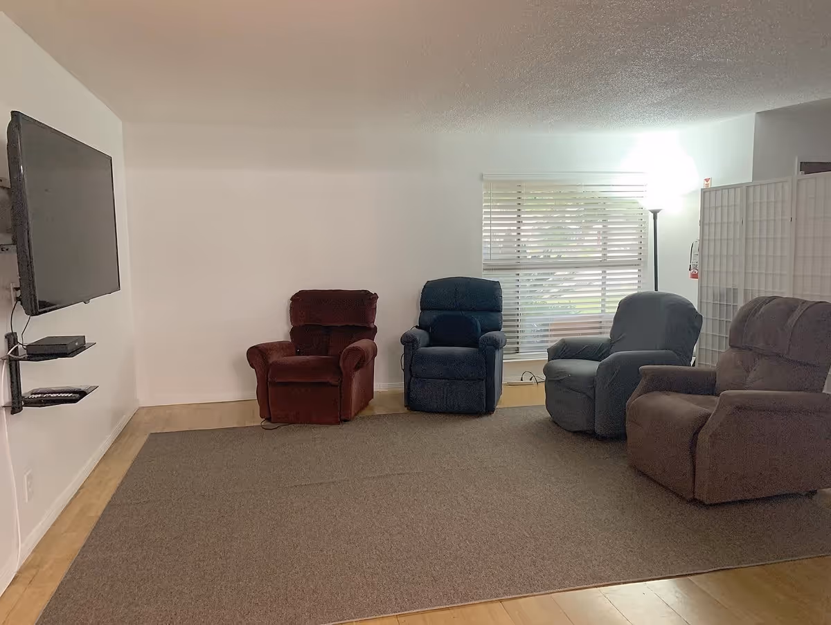 A seating area with four recliner chairs, a wall-mounted TV, and a window with blinds.